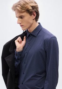 Πουκάμισο σε ναυτικό μπλε χρώμα με μικρές λευκές τελείες, μακριά μανίκια, εφαρμοστή γραμμή και γιακά, σε συνδυασμό με μαύρο σακάκι.