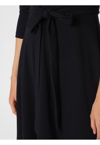 Dunkelblaues Kleid aus einem weichen Stoff, mit einem gebundenen Taillendetail und drei Viertel Ärmeln. Die Textur ist glatt und fließend.