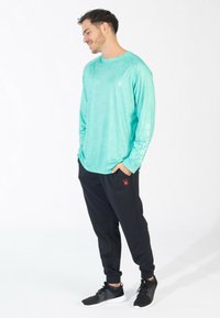 Turkis langærmet skjorte med tekstur, prydet med et trykt logo på brystet og "SPYDER" på ærmet. Sorte joggerbukser med rødt logo.