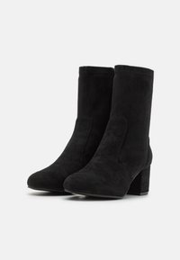 Bottines noires en daim avec un talon bloc, présentant une texture lisse, un bout arrondi et des panneaux latéraux pour un enfilage facile.