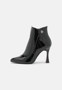 Bottine en cuir verni noir avec un bout pointu, un talon aiguille haut et un accent décoratif en forme de fleur argentée sur le côté.