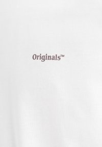 Weißer Stoff mit dem Wort "Originals™" in kleinen, dunkellila gedruckten Buchstaben, in der Mitte der Oberfläche platziert.