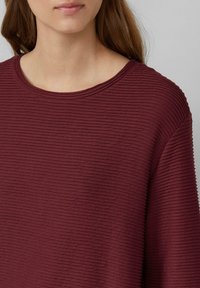 Top testurizzato color bordeaux con linee rigate orizzontali, scollatura ampia e vestibilità rilassata, realizzato in un morbido tessuto a maglia.