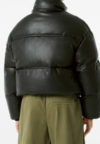 Černá kožená péřová bunda s vysokým límcem, krátkým střihem a prošívanými detaily. Kombinována s olivově zelenými kalhotami s zadní kapsou.