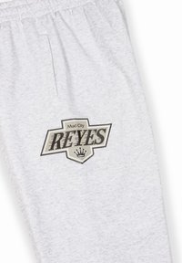 Un pantalon de survêtement gris en tissu doux, arborant un design de logo noir et gris avec le texte "Mud City REYES" et un graphique de couronne.