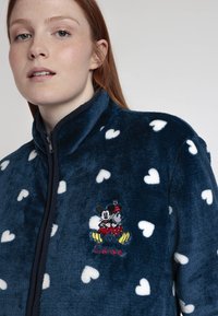 Chaqueta de polar azul marino con patrones de corazones blancos, cuello alto y bordados de Mickey y Minnie Mouse con el texto "Love" en el pecho.