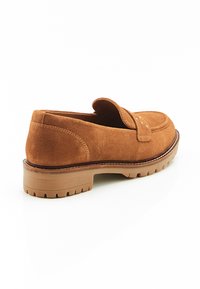 Mocassins en cuir suédé marron avec une semelle en caoutchouc plate et texturée, et une couture décorative sur le dessus. Conception basse avec un devant de style mocassin.