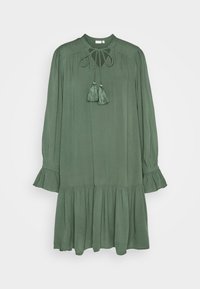 Vestido verde de manga larga hecho de una tela ligera. Presenta un escote redondo con un lazo, borlas y un dobladillo con volantes en capas.