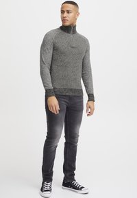 Grå teksturert zip-up genser med høy krage, paret med mørke jeans og svarte joggesko. Har tilpassede ermer og ribbet nederkant.