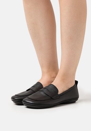 Sorte læderloafers med en glat tekstur, der har en dekorativ rem tværs over overdelen og en lav profil sål.