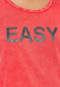Rode T-shirt met een ronde hals en korte mouwen, voorzien van grote zwarte letters die "EASY" over de voorkant spellen. Zacht, textured stof.