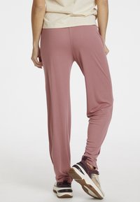 Růžové, lehké, elastické kalhoty s volným střihem, vybavené bočními kapsami a hladkým povrchem, v kombinaci s bílými a hnědými teniskami.