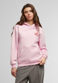 Sudadera rosa en una suave mezcla de algodón con un bolsillo frontal. Presenta un gráfico bordado en rojo. Ajuste cómodo con mangas largas y capucha.