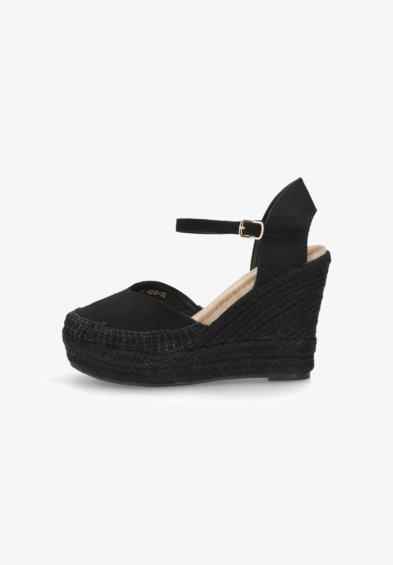 Zapato de esparto negro con cuña, con suela de yute trenzado, punta redondeada y correa en el tobillo. Parte superior de tela suave y detalles texturizados en el talón.