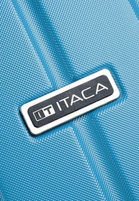 Maleta rígida azul con una superficie texturizada, que presenta líneas diagonales y una placa de logo rectangular negra que dice "IT ITACA".