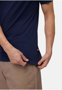 Navyblaues T-Shirt aus weichem Stoff, mit abgerundetem Saum und einem kleinen roten Akzentlogo am unteren Saum. Leicht und eng geschnitten.
