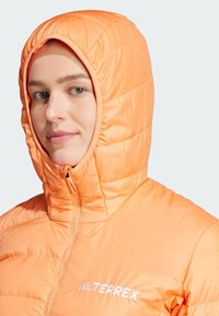 Padded orange hooded jacket with a zipper, featuring a quilted design and white logo. Smooth texture and snug fit around the face.