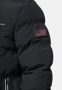 Black puffer jacket with a shiny texture, featuring a zippered pocket and an embroidered American flag patch on the left arm.