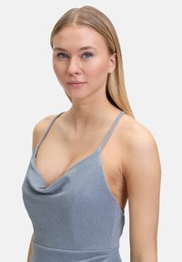 Sukienka z dekoltem w kształcie peleryny w jasnoniebieskim kolorze, z metalicznym połyskiem, na cienkich ramiączkach i dopasowanym gorsetem. Gładka faktura z eleganckim drapowaniem przy dekolcie.