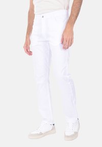 Jeans bianchi in cotone con una vestibilità slim, design a cinque tasche e dettagli di cucitura discreti. Abbinati a sneakers bianche e grigie.