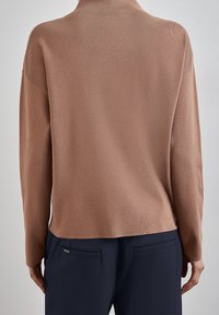 Brun stickad tröja med hög krage, lös passform och strukturerad tyg, tillsammans med marinblå byxor med bakfickor.