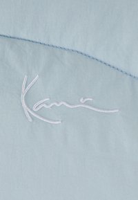 Ljusblått tyg med en slät textur och en vit broderad signaturdesign, accentuerad av en subtil böjd söm.