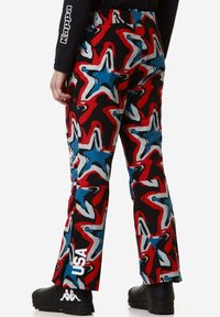 Pantaloni da sci colorati con un audace motivo a stelle in rosso, blu e nero. Comprendono una tasca laterale e un marchio sulla parte inferiore della gamba sinistra.
