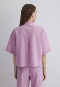 Short-sleeve, collar shirt in light pink with white and purple stripes, featuring a cropped design and back pleat detail.