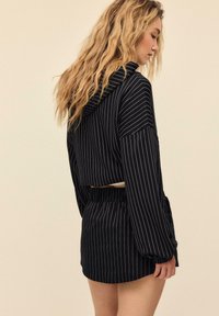 Čierna pruhovaná krátka mikina s dlhými rukávmi a kapucňou, v páre s rovnakou vysokopásovou sukňou. Mäkká látka s voľným strihom.