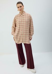 Chemise en flanelle à carreaux jaune pastel et rose, manches longues, fermeture par boutons, portée avec un pantalon large bordeaux et des baskets blanches.