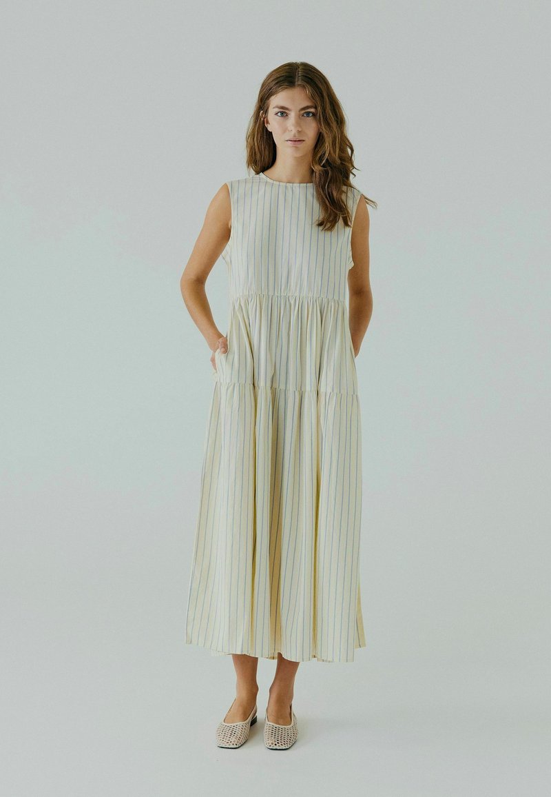 Robe maxi sans manches à volants, de couleur jaune clair avec des rayures verticales bleues. Fabriquée en tissu doux, elle présente une coupe décontractée et des poches latérales.
