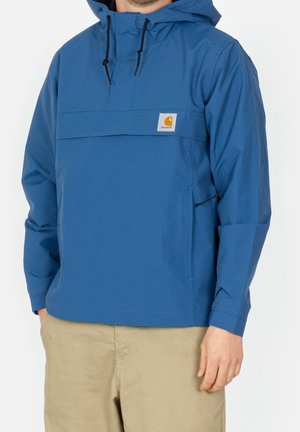 Niebieska kurtka z kapturem, wykonana z gładkiego materiału syntetycznego. Posiada przednią kieszeń na drobiazgi, regulowane sznurki oraz naszywkę z logo.