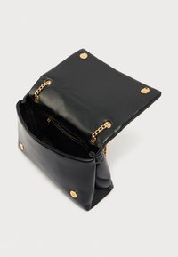 Bolso de mano de cuero negro con cierre de solapa, adornos de cadena dorada y textura suave. El interior incluye un bolsillo con cremallera para mejor organización.