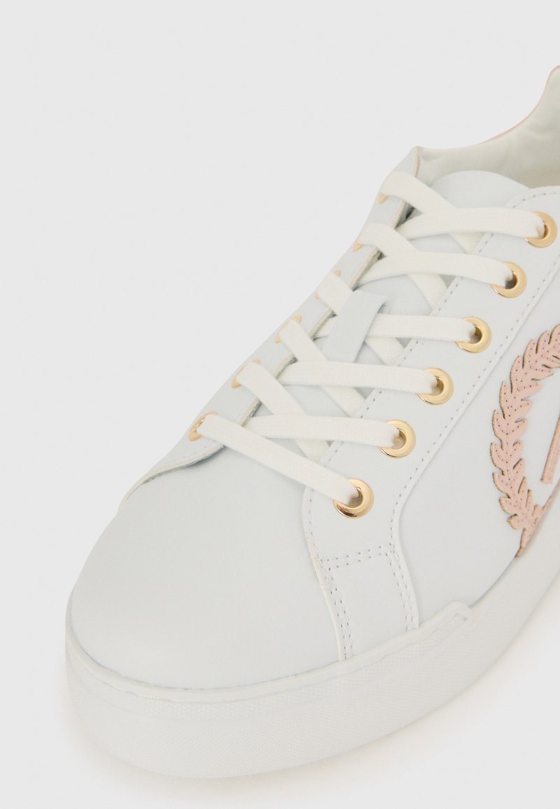 Sneaker bianco con lacci crema, occhielli dorati e un dettaglio di alloro ricamato rosa sul lato.