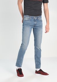 Ljusblå denimjeans med slim fit, med fem fickor och dragkedja. Bärs med en mörkgrå t-shirt och röda sneakers.