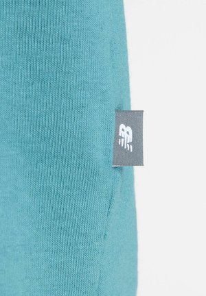 Sinivihreä neulottu kangas, jonka sivusaumassa on pieni harmaa lappu, jossa on valkoisella ommeltu tyylitelty "RB"-logo.