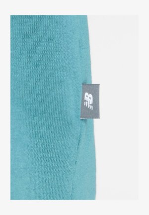 Sinivihreä neulottu kangas, jonka sivusaumassa on pieni harmaa lappu, jossa on valkoisella ommeltu tyylitelty "RB"-logo.