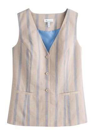 Donna che indossa un gilet beige senza maniche con righe verticali blu e pantaloni abbinati, in piedi con le mani in tasca su uno sfondo chiaro.