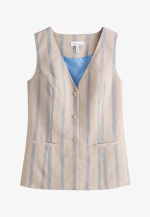 Donna che indossa un gilet beige senza maniche con righe verticali blu e pantaloni abbinati, in piedi con le mani in tasca su uno sfondo chiaro.