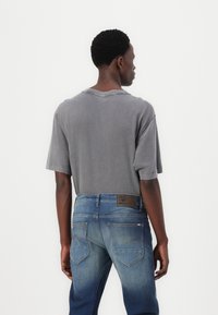 Grå, överdimensionerad t-shirt i bomull med rund halsringning, tillsammans med blå denimjeans som har en gradientfärgskiftning och synliga bakfickor.