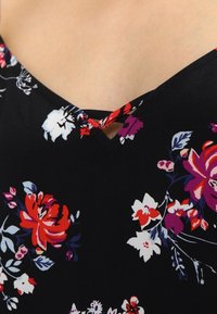 Detalle de un vestido floral con fondo negro y flores en rojo, púrpura y blanco. Escote en V con un pequeño recorte como acento. Textura de tela suave.