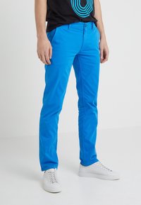 Niebieskie bawełniane chinosy o dopasowanym kroju, z zapięciem na guziki i kieszeniami, zestawione z białymi trampkami. Gładka faktura.