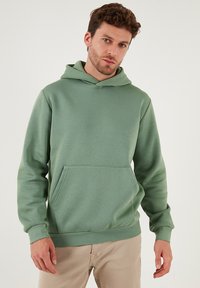 Vihreä huppari pehmeästä kankaasta, jossa etutasku ja resorit hihansuissa, rento ja mukava istuvuus.