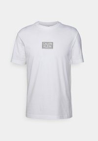 Camiseta de algodón blanca de manga corta, con un logo rectangular gris de Calvin Klein centrado en el frente. Corte regular y escote redondo.