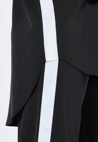 Schwarzes Kleidungsstück mit einer glatten Textur, das einen auffälligen weißen vertikalen Streifen an der Seite und ein geschwungenes Saumdetail aufweist.