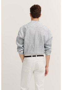 Camicia a righe con linee verticali bianche e nere, con maniche lunghe e colletto standard, abbinata a pantaloni bianchi e una cintura nera intrecciata.