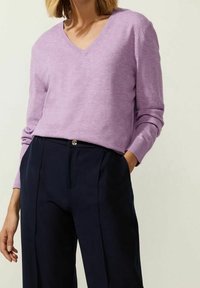 Pull en tricot léger à col en V lavande, avec manches longues et poignets côtelés, associé à un pantalon taille haute bleu marine.