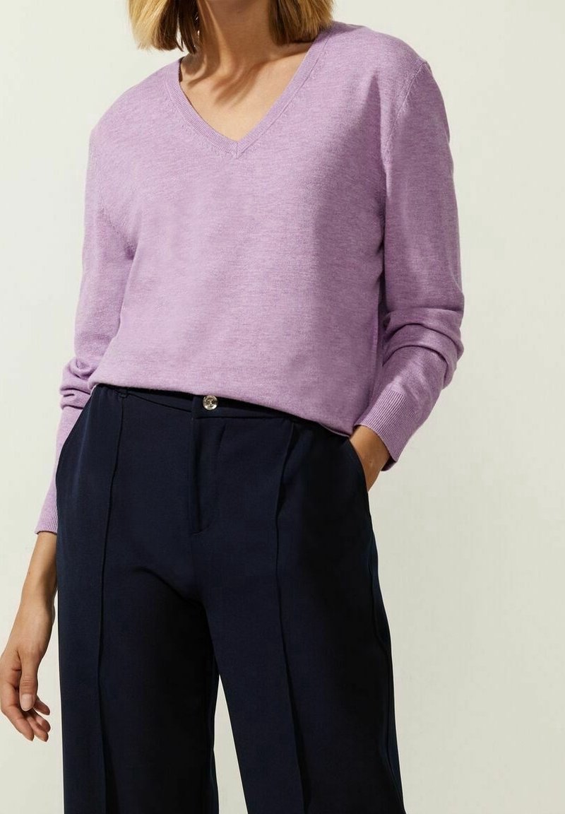 Pull en tricot léger à col en V lavande, avec manches longues et poignets côtelés, associé à un pantalon taille haute bleu marine.