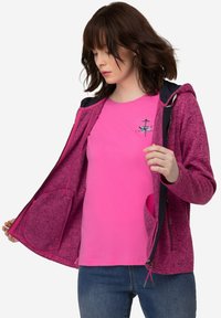 Fleece zip-up jacka i rosa med ett texturerat mönster, med en kontrasterande huva, två framfickor och en rosa t-shirt under.