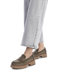 Mocasines de ante verde aceituna con un marcado detalle de costura, una suela de color marrón acolchada y gruesa, y un ligero tacón, combinados con unos vaqueros de denim gris claro.